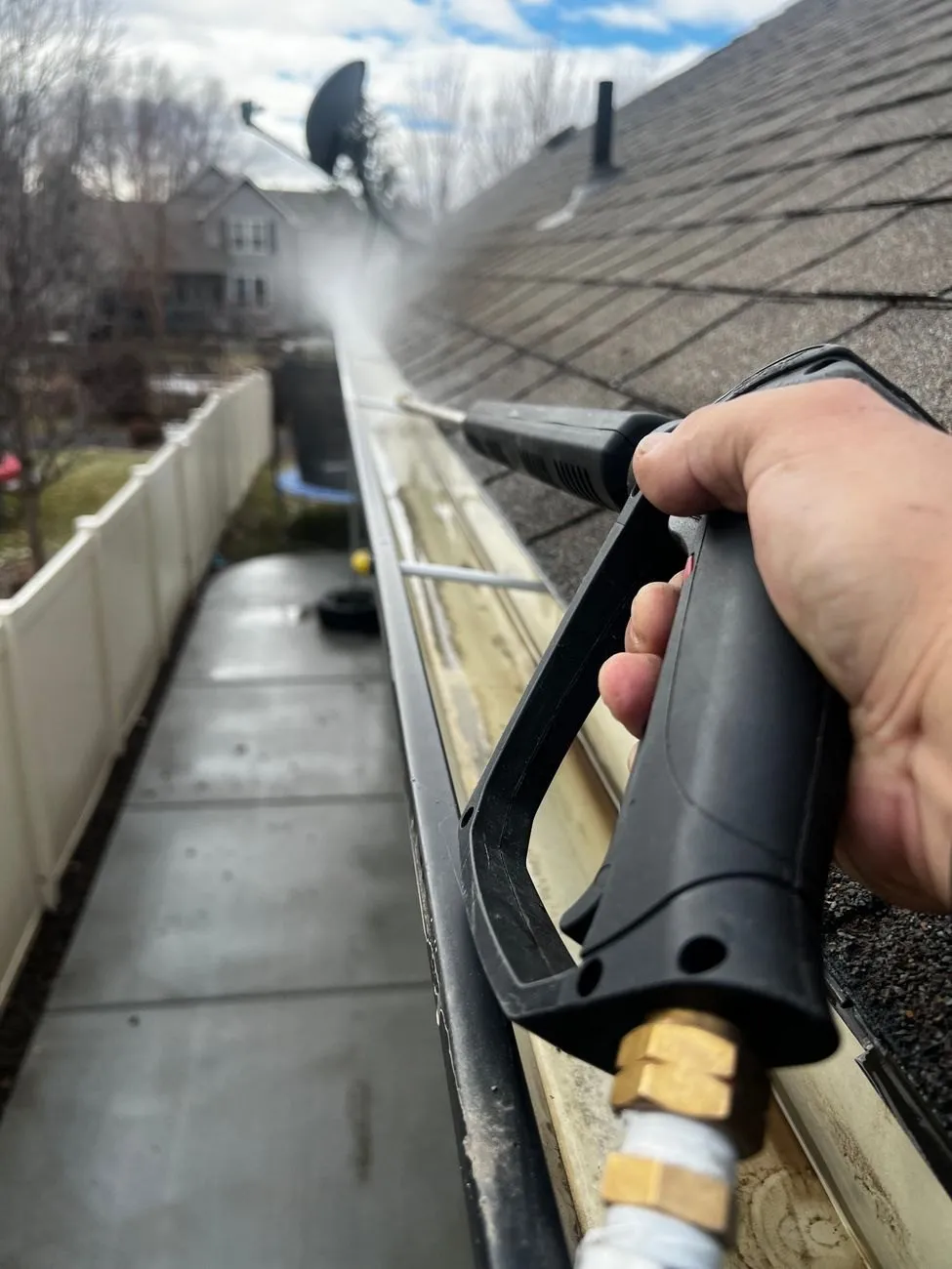 A hand holding a water lance along a gutter run, washing out the last of the silt