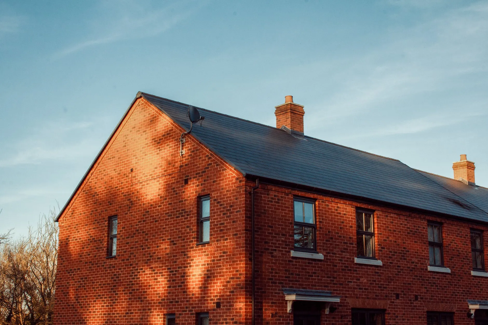The gable end of a red-brick semi-detached house with a slate roof and black gutter